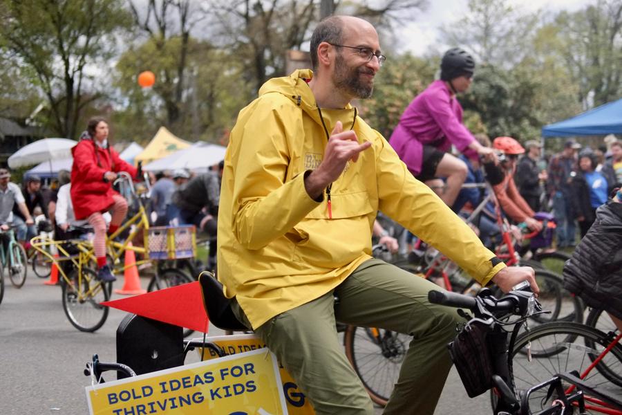 rob riding his bike and throwing the shaka hand sign, with his yard sign on his bike
