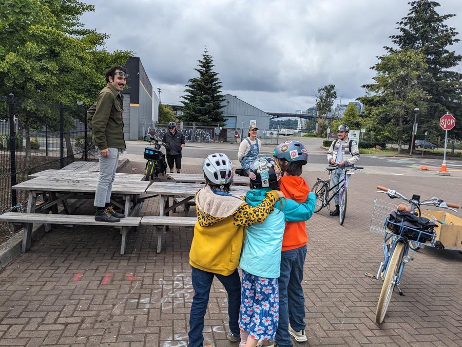 three kids hugging while someone speaks standing on a table